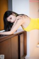 A woman in a yellow dress leaning on a counter.