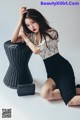 A woman sitting on the ground next to a wicker chair.