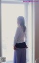 A woman standing in front of a window looking out the window.