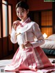 A woman in a pink and white hanbok sitting on a bed.