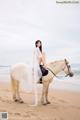 A woman riding on the back of a white horse on a beach.