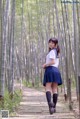 A woman in a school uniform walking down a path in a bamboo forest.