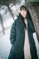 A woman leaning against a tree in the snow.