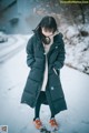 A woman standing in the snow wearing a long black coat.