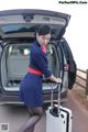 A woman in a blue dress with a suitcase in the trunk of a car.