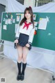 A woman in a school uniform posing in front of a blackboard.