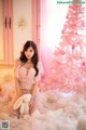 A woman sitting in front of a pink christmas tree holding a teddy bear.