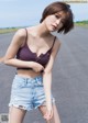 A woman in a purple top and denim shorts posing on a road.