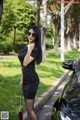 A woman in a black dress standing next to a black car.