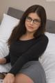 A woman wearing glasses sitting on a bed.