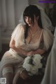 A woman in a wedding dress sitting on a chair with a bouquet of flowers.