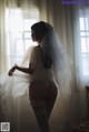 A woman in a wedding dress standing in front of a window.