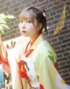 A woman in a yellow and red kimono holding a plant.