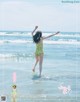 A woman in a green and white polka dot bathing suit jumping in the ocean.