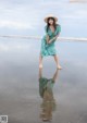 A woman in a green dress and straw hat standing on a beach.