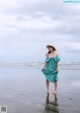 A woman in a green dress and straw hat standing on the beach.