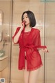 A woman in a red robe standing in a bathroom.